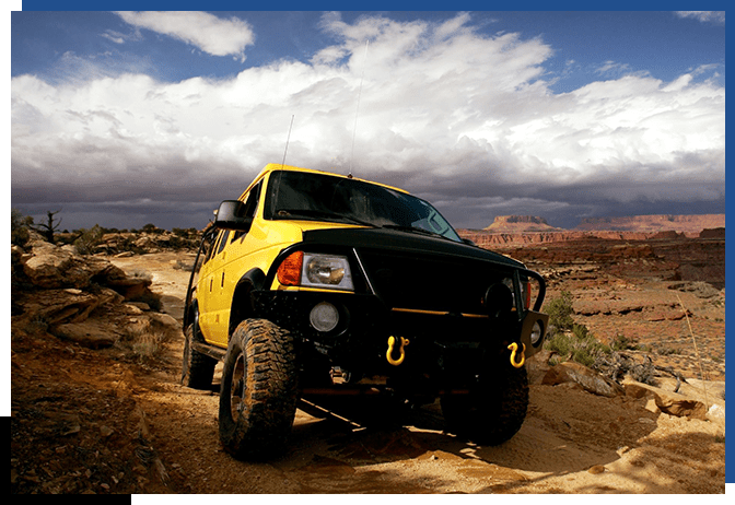 A yellow truck is parked on the side of a dirt road.