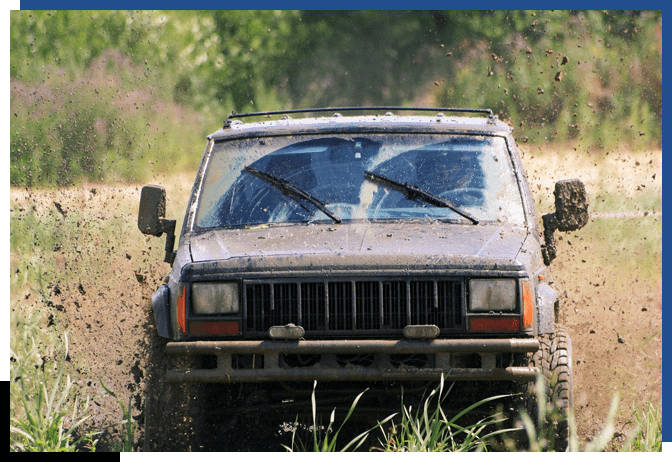 A jeep driving through mud on the side of a road.