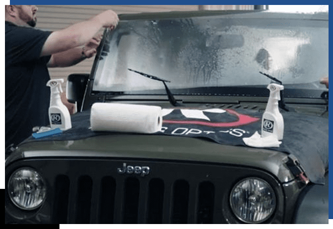 A person is working on the windshield of a jeep.